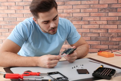 Photo of Technician repairing broken smartphone at table in workshop