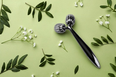 Photo of Metal face roller and flowers on green background, flat lay