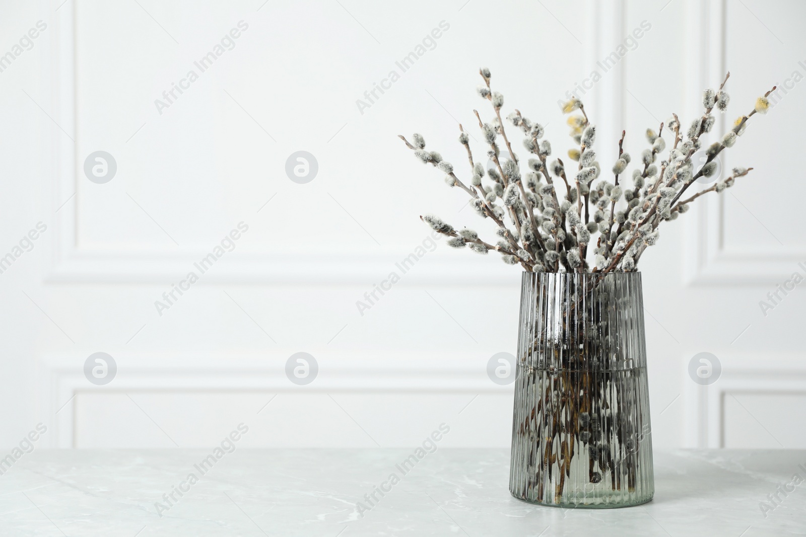 Photo of Beautiful pussy willow branches in glass vase on light grey marble table, space for text