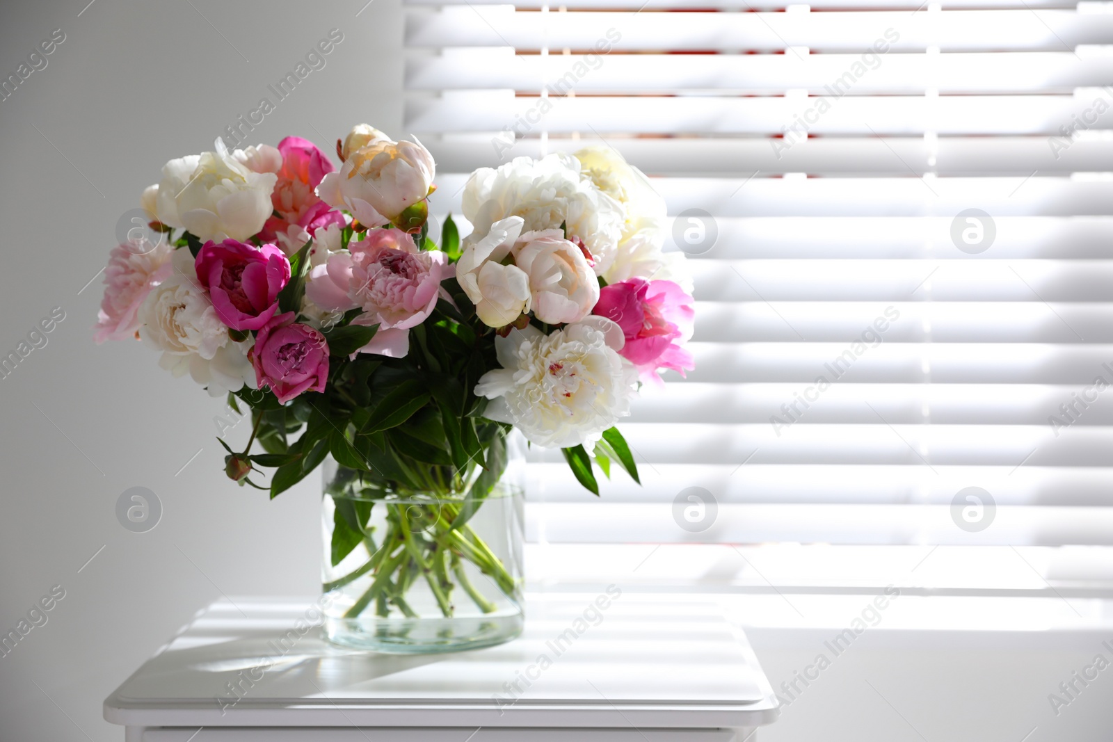 Photo of Beautiful peonies in vase on table near window indoors. Space for text