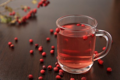 Cup with hawthorn tea and berries on wooden table, closeup. Space for text