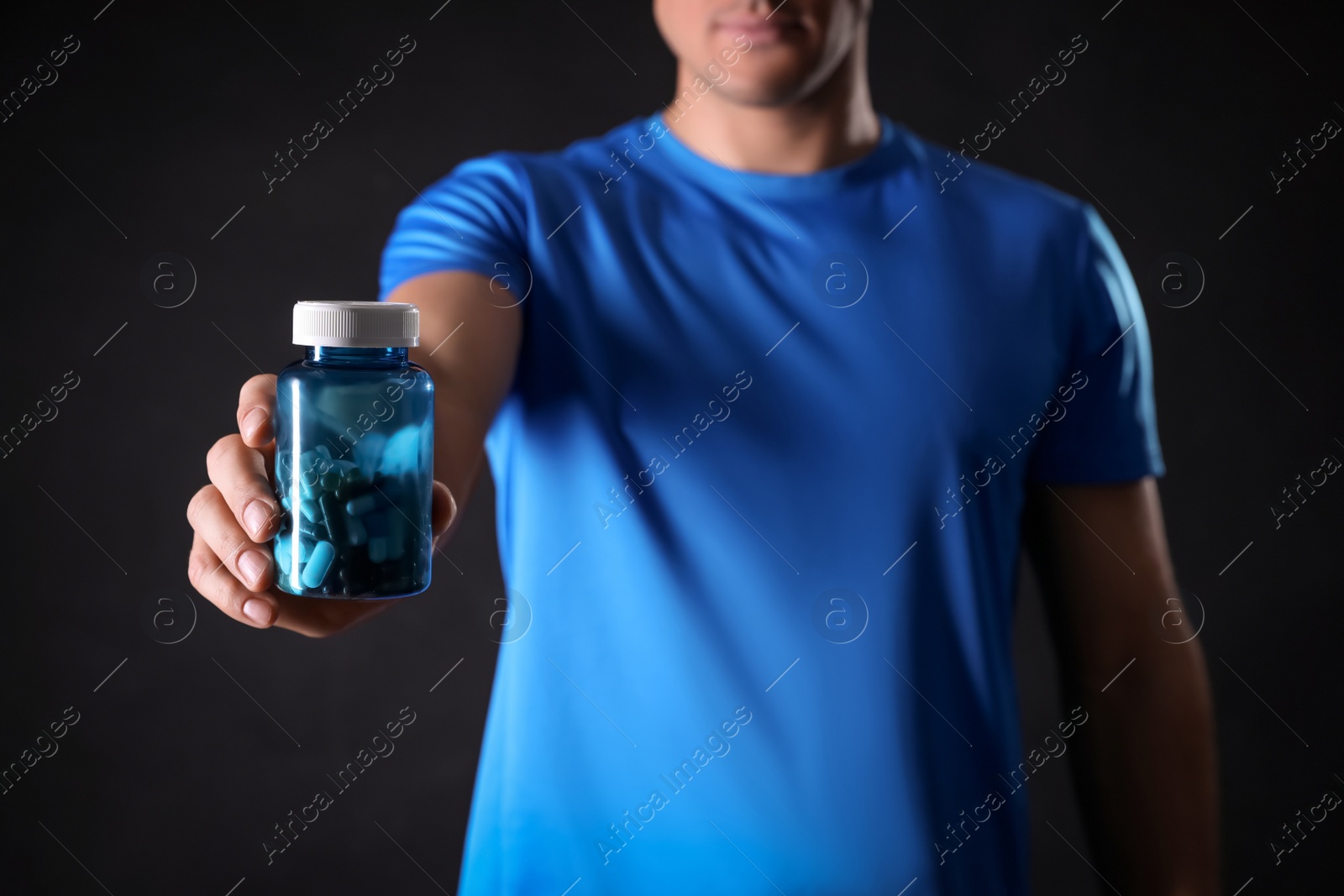 Photo of Man with bottle of pills on black background, closeup. Doping concept