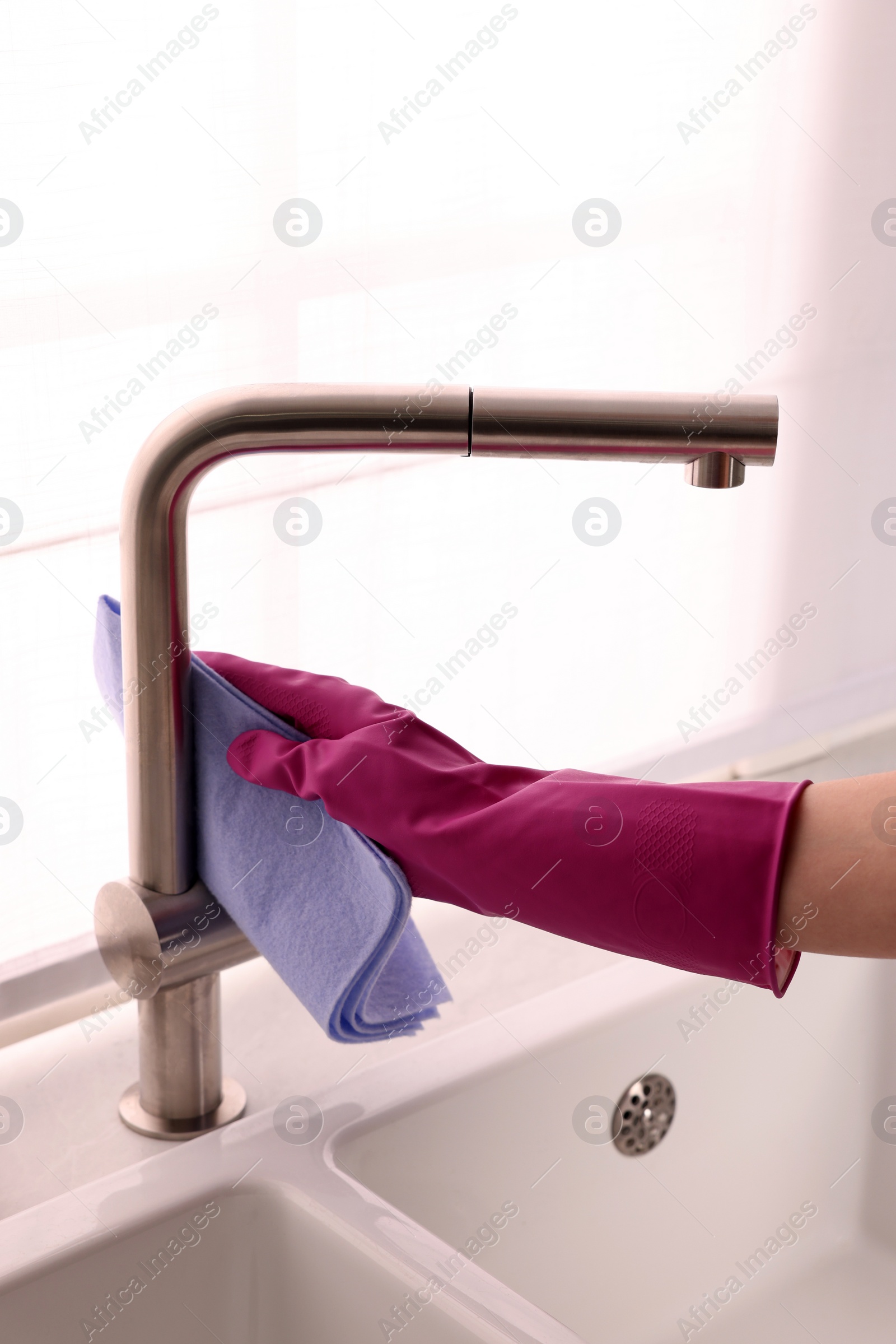 Photo of Woman in gloves cleaning faucet of kitchen sink with rag, closeup