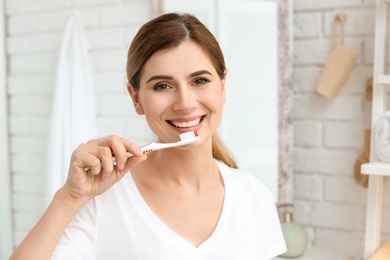 Photo of Young woman brushing her teeth indoors