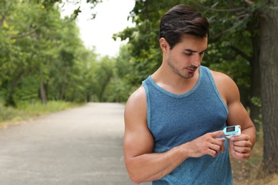 Young man checking pulse with medical device after training in park. Space for text