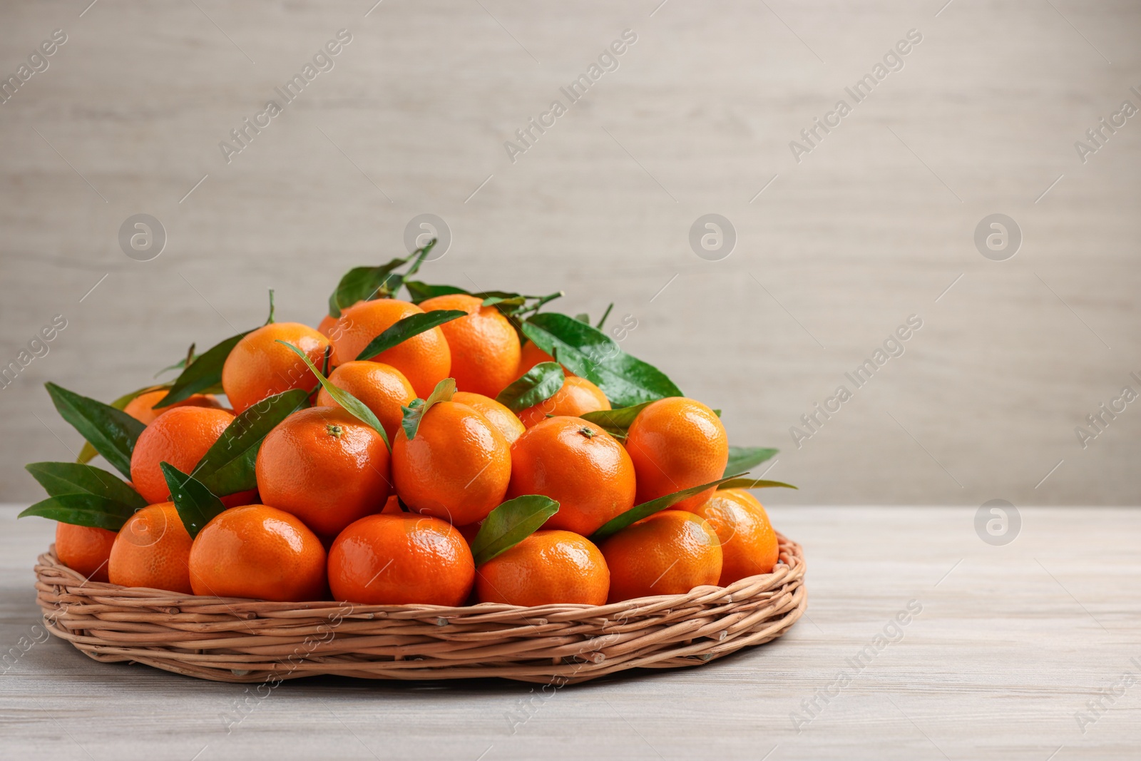 Photo of Fresh ripe juicy tangerines and green leaves on white wooden table, space for text