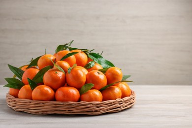 Fresh ripe juicy tangerines and green leaves on white wooden table, space for text