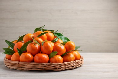 Photo of Fresh ripe juicy tangerines and green leaves on white wooden table, space for text