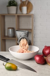 Metal meat grinder with chicken mince and products on light grey table indoors