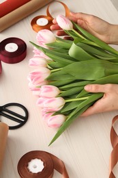 Woman making bouquet of beautiful fresh tulips at white wooden table, closeup