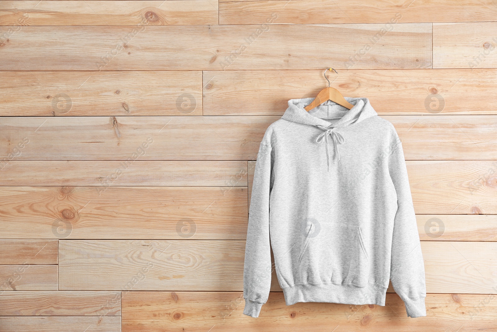 Photo of New hoodie sweater with hanger on wooden wall. Mockup for design