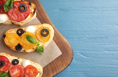 Photo of Board with delicious tomato bruschettas on blue wooden background, top view. Space for text