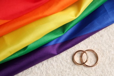 Rainbow LGBT flag and wedding rings on white background, top view