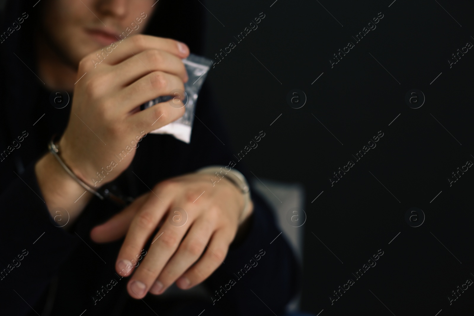 Photo of Man detained in handcuffs holding bag with drug against dark background, space for text. Criminal law