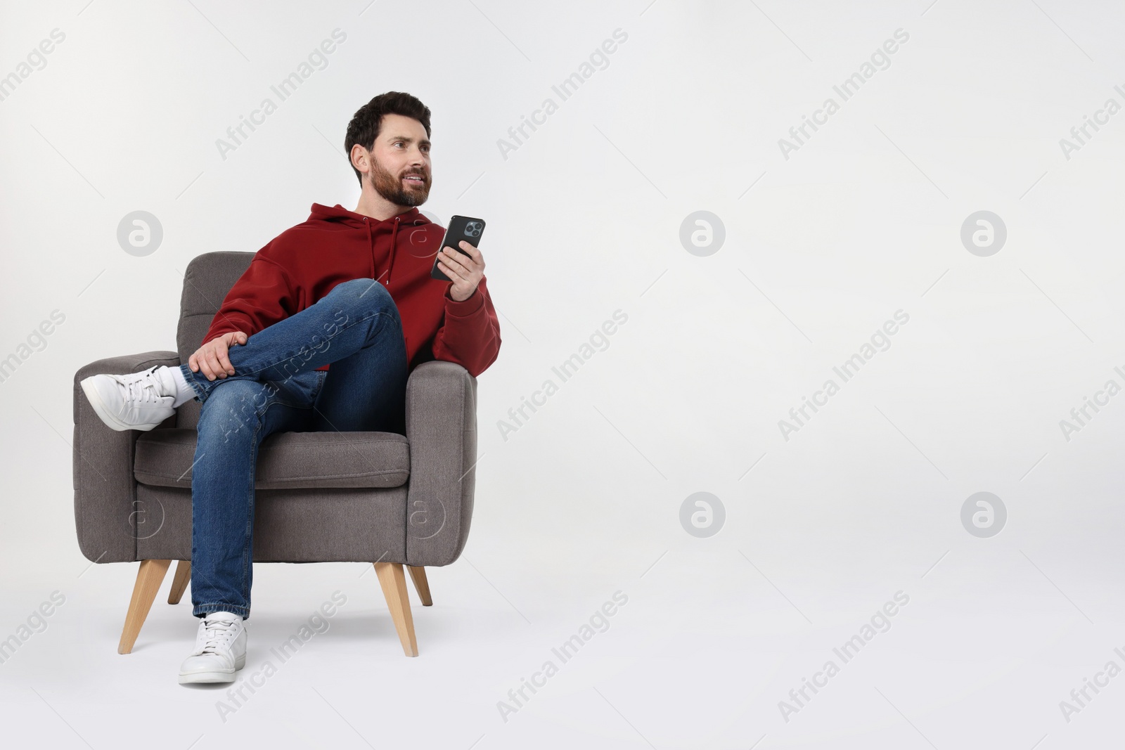 Photo of Happy man with smartphone sitting on armchair against white background. Space for text