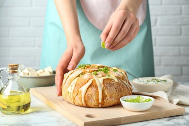 Photo of Woman adding green onion onto freshly baked bread with tofu cheese at white marble table, closeup
