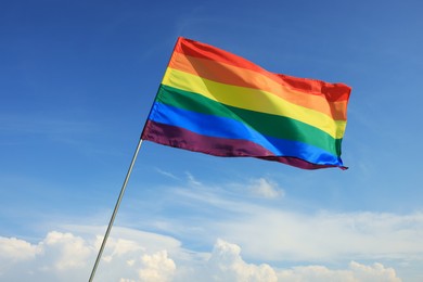 Photo of Woman holding bright LGBT flag against blue sky, closeup
