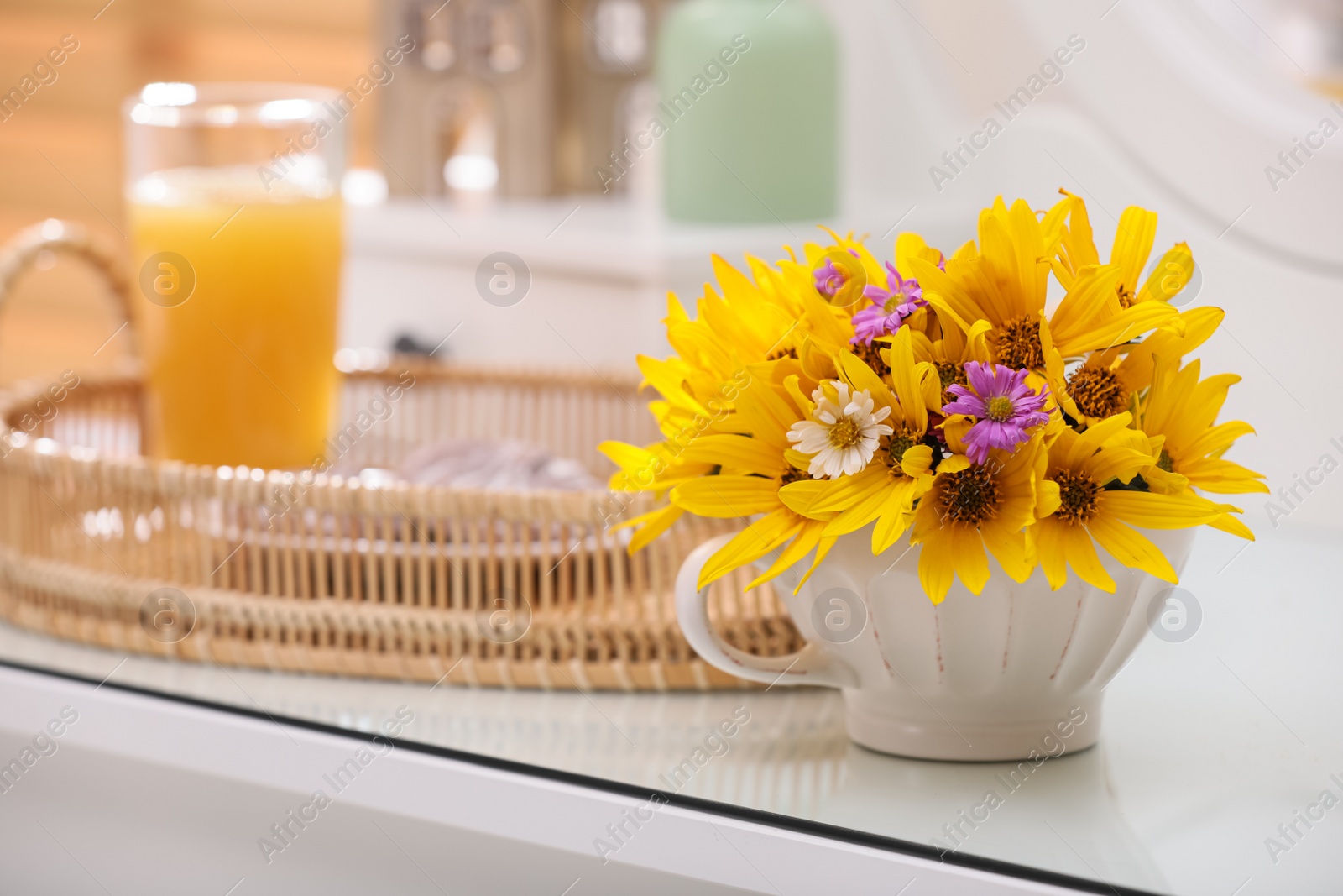 Photo of Beautiful bright flowers in cup on white table. Space for text