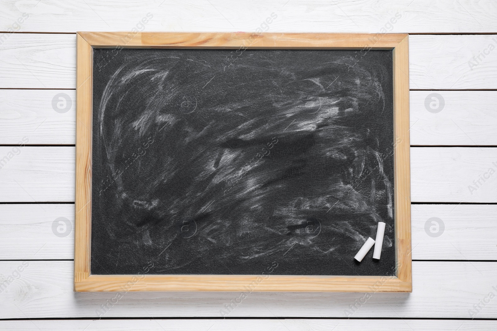 Photo of Blackboard with pieces of chalk on white wooden background, top view. Space for text