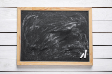 Blackboard with pieces of chalk on white wooden background, top view. Space for text