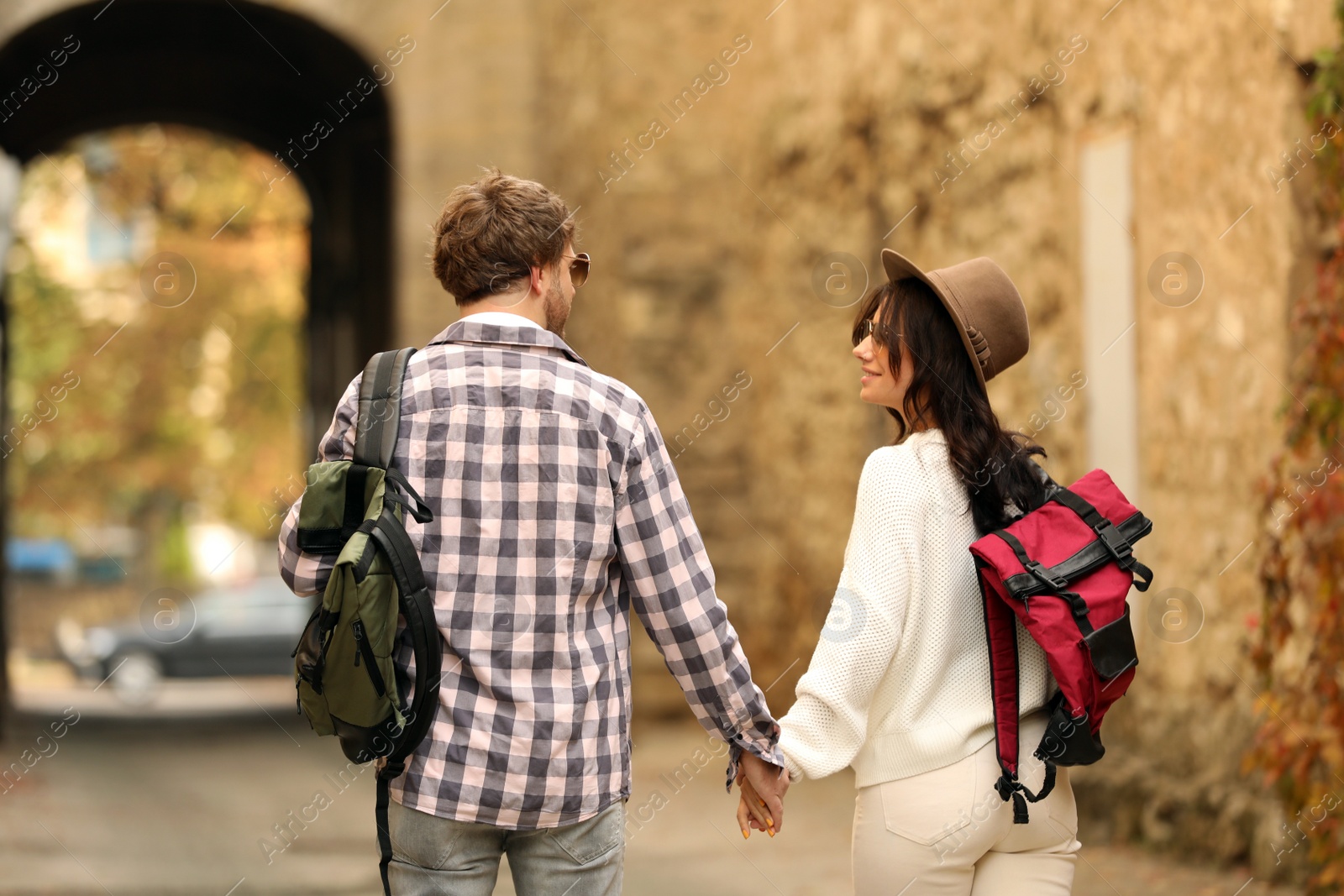 Photo of Couple of travelers with backpacks on city street, back view