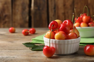 Photo of Sweet red cherries in bowl on wooden table, space for text