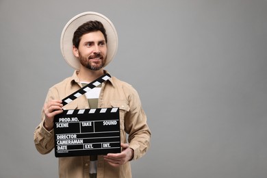 Photo of Smiling actor holding clapperboard on grey background, space for text