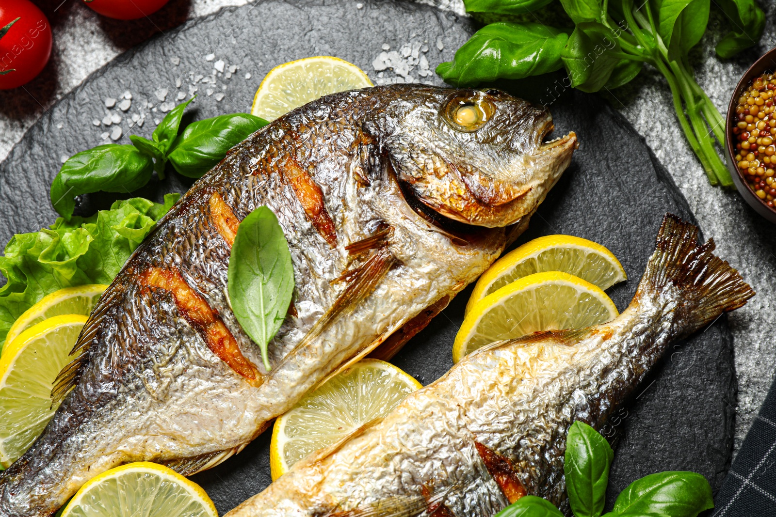 Photo of Delicious roasted fish with lemon on slate plate, closeup