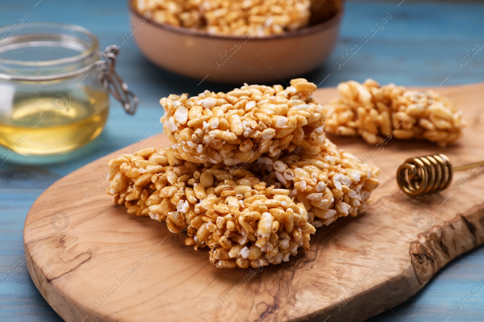 Photo of Board with puffed rice bars (kozinaki) on light blue wooden table, closeup