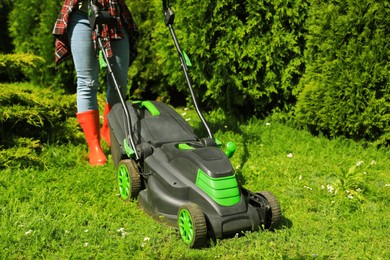 Photo of Woman cutting grass with lawn mower in garden on sunny day, closeup