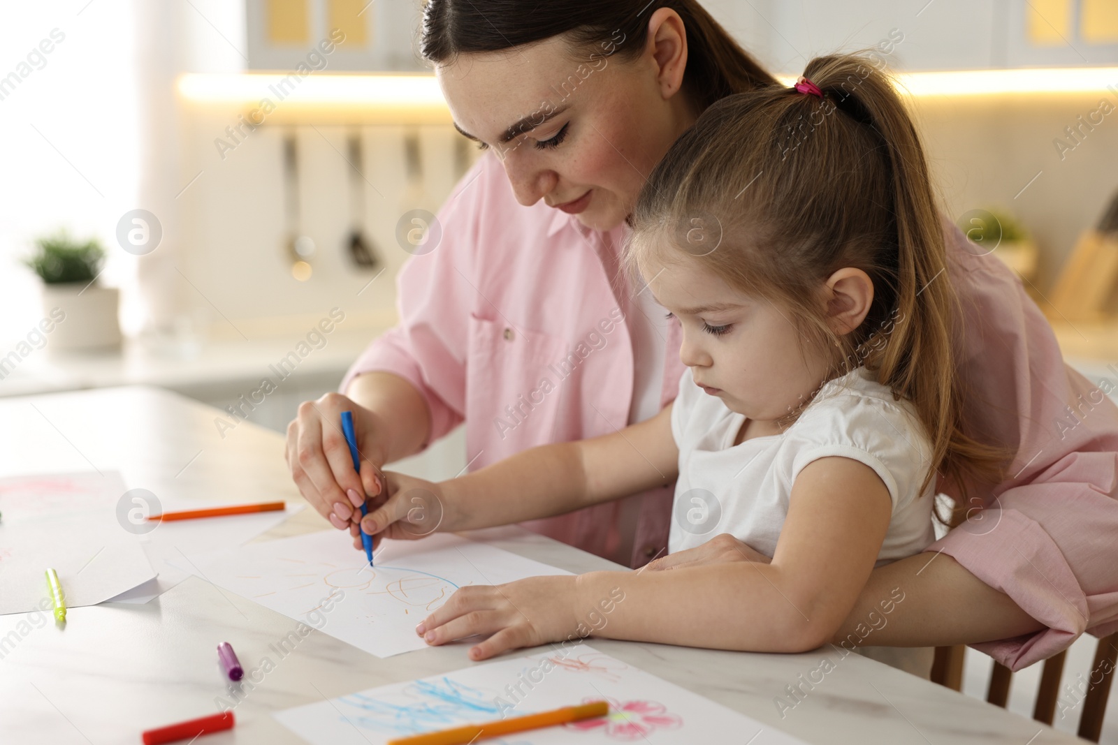 Photo of Mother and her little daughter drawing with colorful markers at table in kitchen