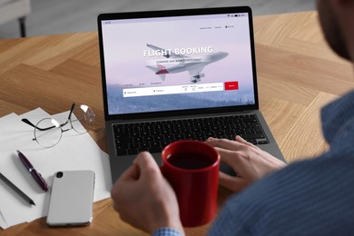 Image of Man using laptop to book flight at wooden table, closeup