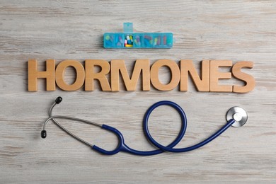 Photo of Word HORMONES made with wooden letters, stethoscope and pill container on table, flat lay