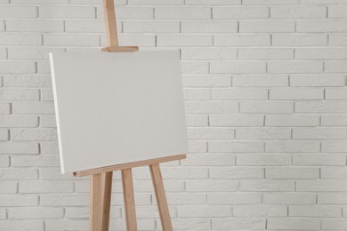 Wooden easel with blank canvas near white brick wall. Space for text