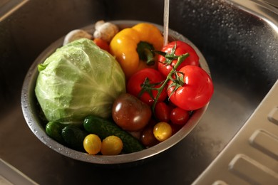 Photo of Washing different vegetables with tap water in metal colander inside sink