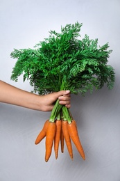Photo of Woman holding ripe carrots on light background, closeup