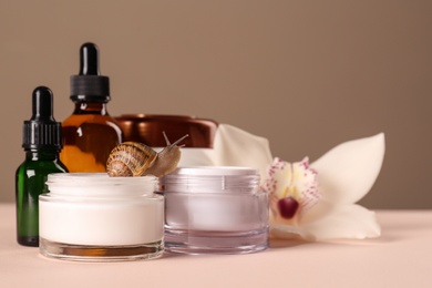 Photo of Organic cosmetics made with mucin, snail and beautiful flower on table. Space for text