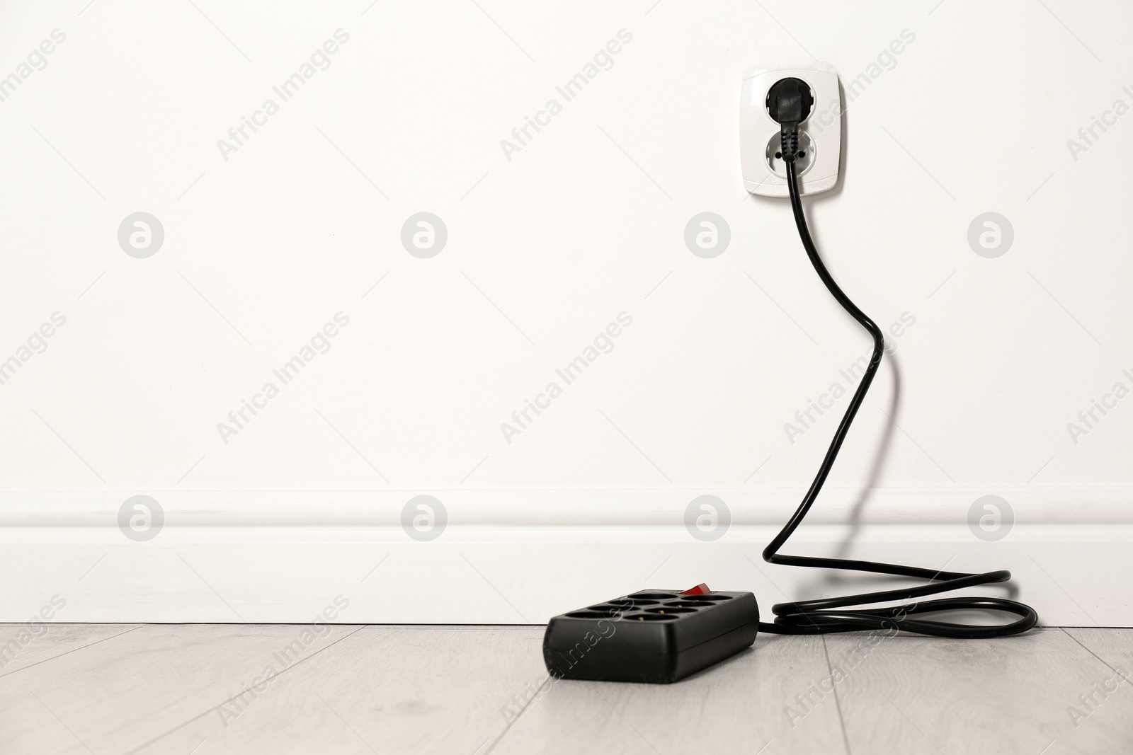 Photo of Extension cord with power plug in socket indoors, space for text. Electrician's professional equipment