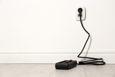 Extension cord with power plug in socket indoors, space for text. Electrician's professional equipment