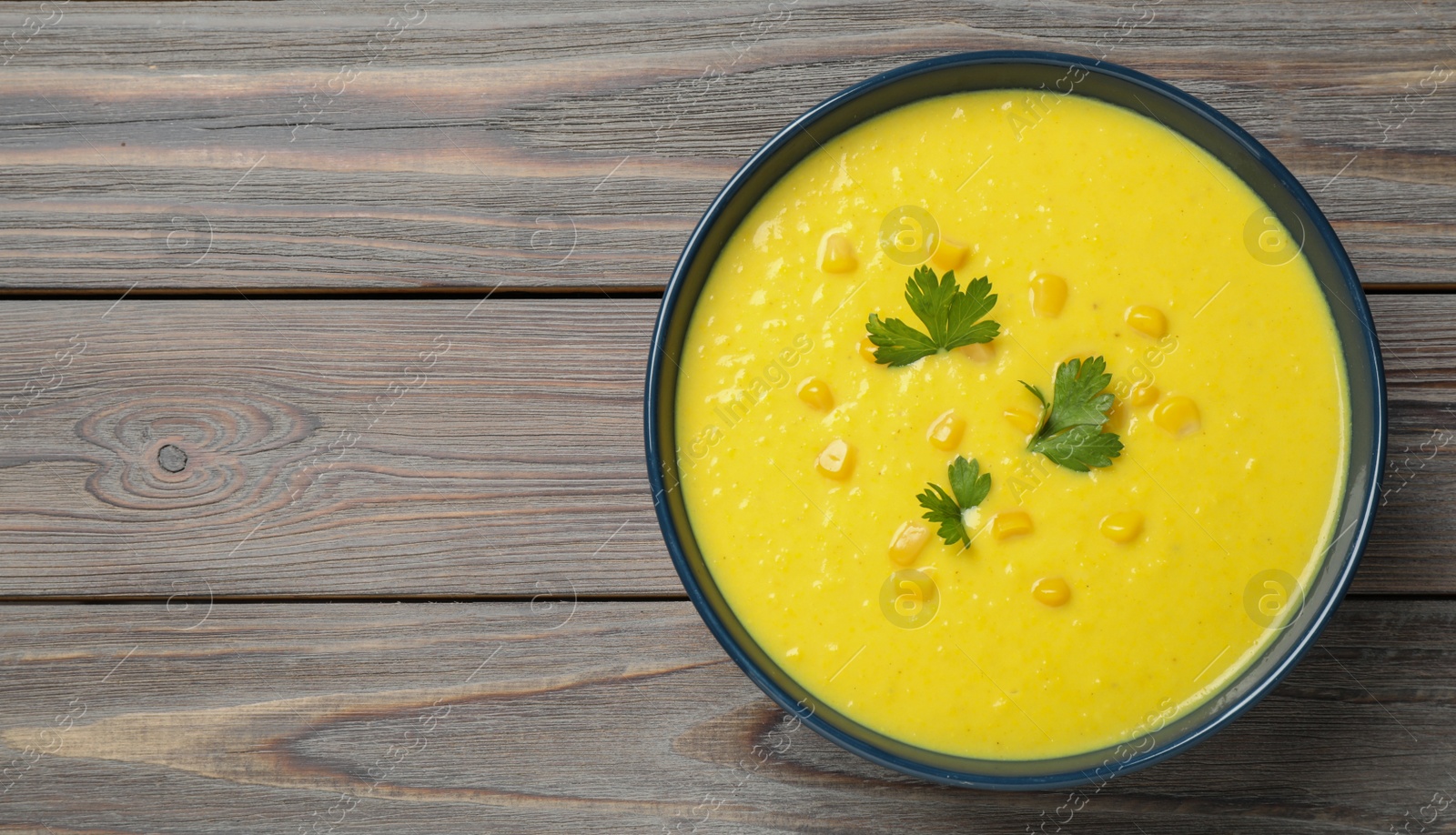 Photo of Delicious creamy corn soup served on wooden table, top view. Space for text