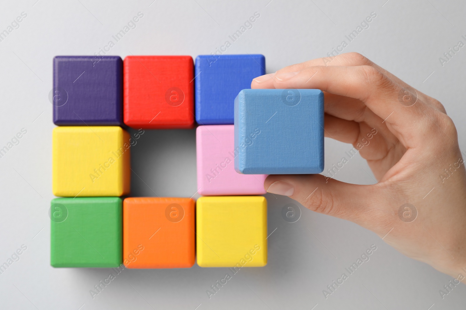 Photo of Woman holding light blue wooden cube over table with others, top view. Management concept