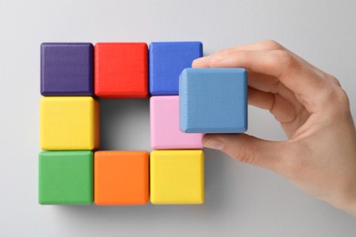 Photo of Woman holding light blue wooden cube over table with others, top view. Management concept