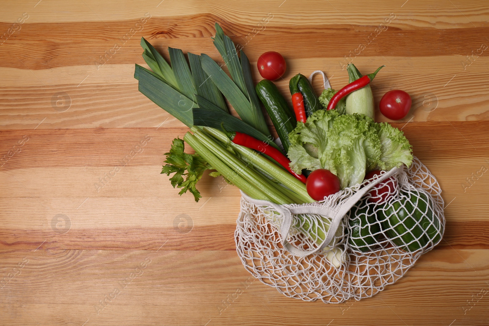 Photo of Net bag with vegetables on wooden background, top view