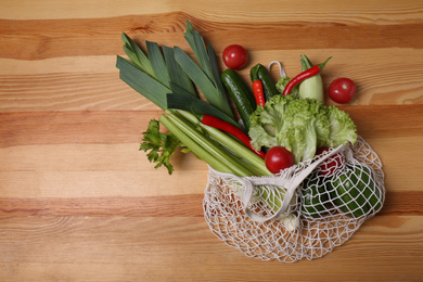 Photo of Net bag with vegetables on wooden background, top view