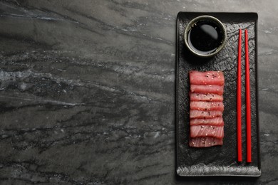 Photo of Tasty sashimi (pieces of fresh raw tuna with sesame seeds) and soy sauce on black marble table, top view. Space for text