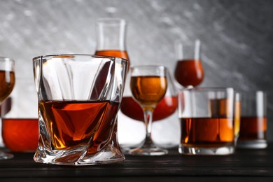 Photo of Different delicious liqueurs in glasses on dark wooden table