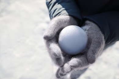 Woman holding snowball outdoors on winter day, closeup. Space for text