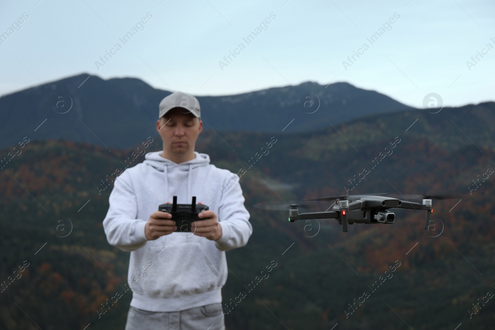 Photo of Young man operating modern drone with remote control in mountains