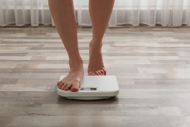 Photo of Woman stepping on floor scales indoors, closeup. Weight control