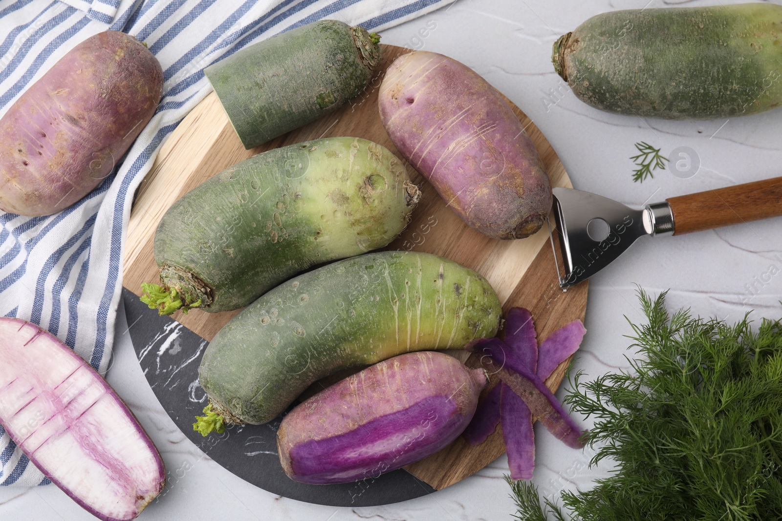 Photo of Daikon radishes, dill and peeler on white textured table, flat lay